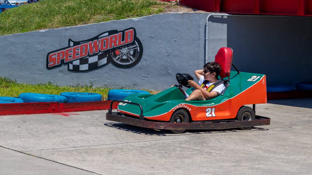 Boy on green and orange cart with speed world sign on the track wall