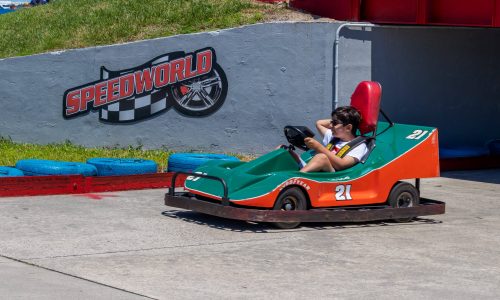 Boy on green and orange cart with speed world sign on the track wall